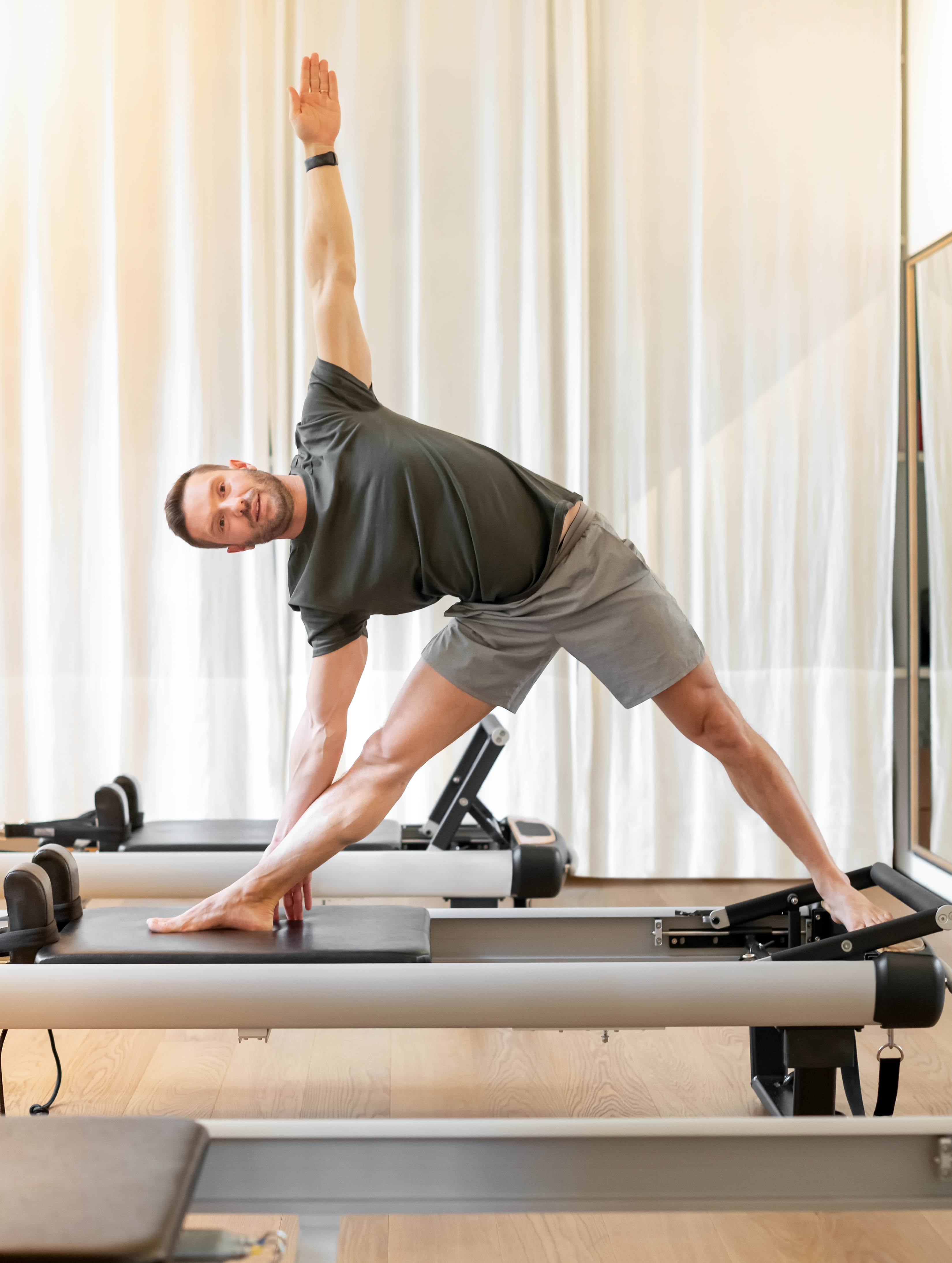 Man performing a triangle pose on a Pilates reformer